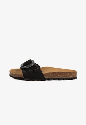 Sandale à glissière en suede noir avec une boucle circulaire noire, semelle en liège et semelle en caoutchouc texturé. Design plat, style ouvert à l'avant.