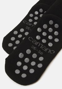 Chaussettes noires présentant une surface texturée avec des points de grip en caoutchouc gris, affichant des marquages de taille 35-38 et un nom de marque en gris.