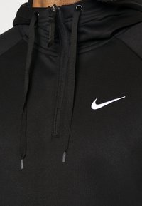 Svart sportig hoodie med dragkedja i nacken, justerbara snoddar och en vit Nike-logga. Slät tyg och kontrasterande axelpaneler.
