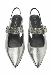 Srebrne buty typu slingback z wydłużonym noskiem, metaliczną teksturą oraz szerokim paskiem z okrągłymi wycięciami i klamrą.