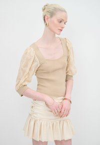 Body color beige con scollo quadrato e maniche a sbuffo in pizzo trasparente, abbinato a una minigonna crema arricciata con orlo a volant.