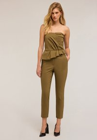 Top peplum senza spalline di colore verde oliva, con un design drappeggiato e un accento di rouches, abbinato a pantaloni su misura slim-fit. Tacchi alti neri.