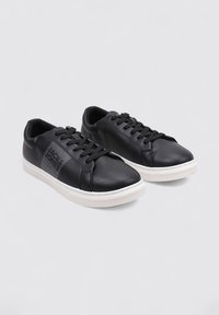 Zapatillas de cuero negro con un acabado suave, suela de goma blanca y acentos laterales en contraste. Presentan un diseño tradicional de cordones.