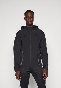 Zwarte jas met ritssluiting en capuchon, gemaakt van lichtgewicht materiaal. Voorzien van een logo op de borst en zijritszakken. Gestructureerde manchetten en zoom.