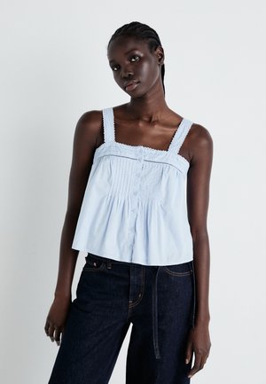 Light blue spaghetti strap top with lace trim, featuring a front button closure and gathered texture. Worn with dark denim jeans.