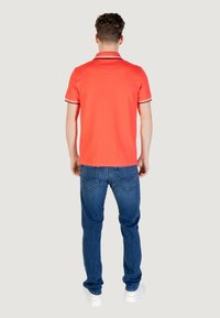 Polo rosso a maniche corte, con strisce bianche e nere sul colletto e sulle maniche. Abbinato a jeans blu e sneaker bianche.