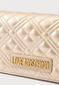 Portafoglio in pelle trapuntata dorata con superficie testurizzata e una prominente placca con il logo "LOVE MOSCHINO" in oro. Forma rettangolare con motivo cucito.