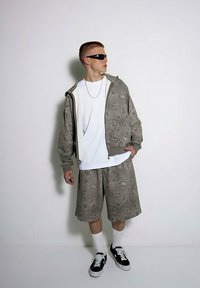 Szary zestaw z nadrukiem paisley składający się z bluzy i szortów, biała koszulka pod spodem, czarne okulary przeciwsłoneczne, czarne sneakersy z białymi akcentami, białe skarpetki.