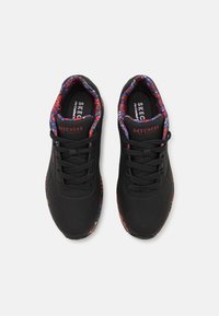 Chaussures de sport noires avec une surface texturée, dotées d'accents floraux colorés sur le col et la semelle, et de lacets noirs.