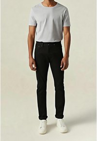 Grå t-shirt med korta ärmar kombinerad med svarta figurnära byxor och vita sneakers, som framhäver en avslappnad stil mot en enfärgad bakgrund.