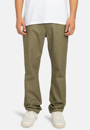 Olive green cotton pants with straight legs, featuring a zip fly and side pockets, paired with white sneakers for contrast.