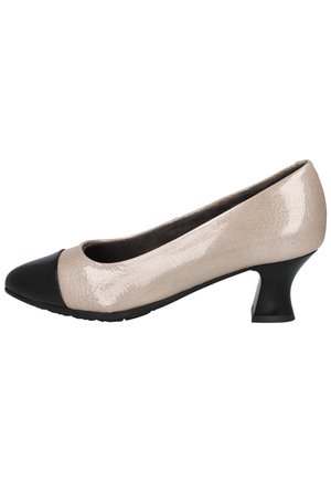 Zapato de charol beige con tacón bajo, puntera redondeada negra y tacón corto y curvado.