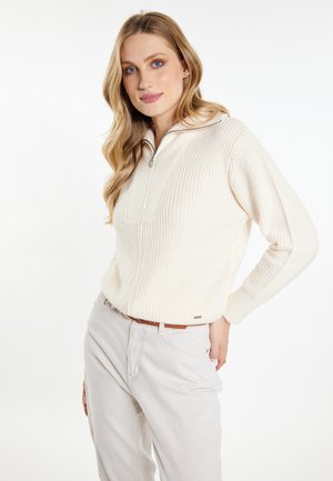 Lichtcreme gebreide pullover met een half-rits kraag, geribbelde textuur en lange mouwen. Gepaard met lichtgrijze broek en een bruine riem.