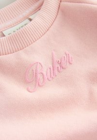 Jasnoróżowy sweter z teksturowanej tkaniny, z ryflowanym dekoltem i haftem "Baker" w lekko ciemniejszej różowej nitce.