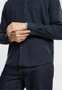 Marineblauwe overhemdd met lange mouwen, voorzien van een contrasterende grijze manchet, een zachte textuur en een relaxte pasvorm, gecombineerd met donkere jeans.