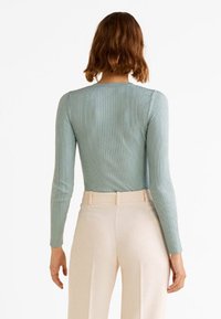 Body a maniche lunghe, in maglia a coste di colore blu chiaro, con scollatura rotonda e design aderente. Indossato con pantaloni a vita alta di colore crema.