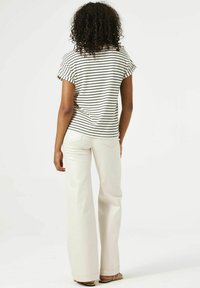 Gestreept T-shirt met korte mouwen in off-white en zwart; gecombineerd met hoge, wijde crèmekleurige broeken. Heeft uitsparingen op de mouwen van het shirt.