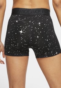 Cortos atléticos negros con un patrón de estrellas y puntos blancos, cinturilla elástica con un sutil logo "NIKE PRO", llevados por una persona de pie.