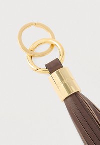 Pruun nahast võtmehoidja tutiga, kuldse metallist riistvara, ümmargused rõngad ja metallkomponendil graveeritud brändiloogo.