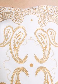 Witte stof met ingewikkelde gouden paisley- en decoratieve patronen, gladde textuur, met een symmetrisch ontwerp inclusief cirkelvormige accenten.