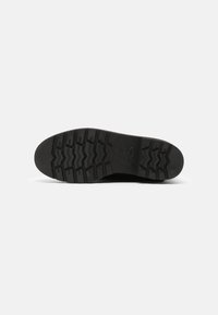 Suela de zapato de goma negra con profundos surcos y patrones en zigzag, con un diseño plano que ofrece tracción y durabilidad.