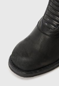 Bota de couro preta com biqueira reforçada e seção de tornozelo acolchoada, mostrando textura detalhada e costura na sola e parte superior.