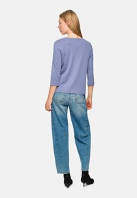 Hellblaue, lockere Jeans kombiniert mit einem helllila Oberteil mit drei Viertelärmel, das aus einem glatten Stoff gefertigt ist und minimale Details aufweist.