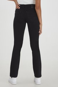 Pantalones acampanados negros con cintura alta, fabricados en tejido elástico. Presentan bolsillos traseros y detalles de costura sutiles. Se combinan con zapatillas blancas.