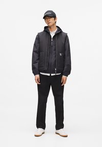 Melna pildīta veste ar kapuci, kārtojama virs pelēkā džempera un baltas krekla. Apvienota ar melnām biksēm un baltām kedām. Melnā cepure ar logotipu.