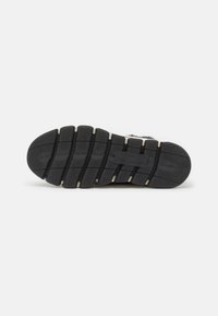 Svart gummi såle til sneakers med en strukturert overflate, som har flere spor og en hvit aksentstripe. Robust med godt grep.
