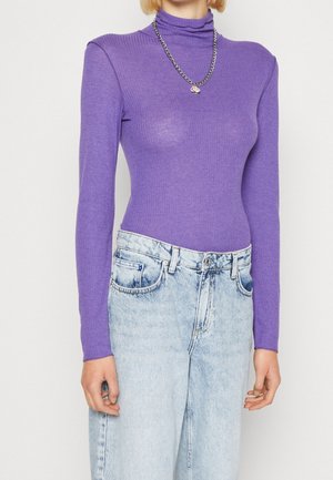 Personne portant un col roulé violet ajusté à manches longues et un jean taille haute clair avec un collier chaîne argenté.