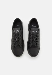 Mustat nahkaiset tennarit, joissa on sileä pinta, pyöristetty kärki ja litteä kumipohja. Varustettu mustilla nauhoilla ja merkinnällä, jossa lukee "A|X".