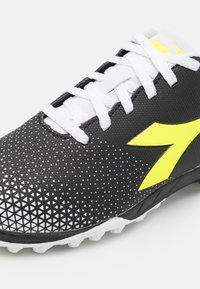 Scarpa da calcio nera con tomaia testurizzata caratterizzata da un motivo triangolare, lacci bianchi e un logo in un vivace giallo. Design classico con tacchetti.
