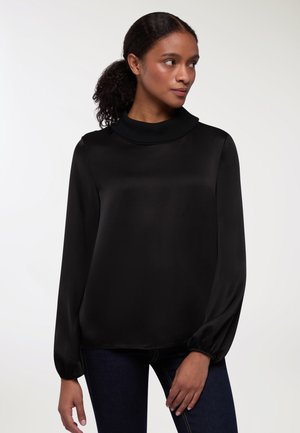 Blusa nera a maniche lunghe con colletto alto e a costine; realizzata in tessuto morbido con vestibilità rilassata e polsini arricciati. Dettagli testurizzati sul collo.