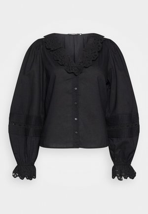 Schwarze Bluse mit einem gerüschten Spitzenkragen, puffigen Ärmeln und dekorativen Akzenten an den Manschetten. Verfügt über eine durchgehende Knopfleiste und strukturierte Details.
