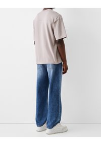 T-shirt in cotone grigio chiaro a maniche corte, abbinata a jeans denim blu slavato dai taglio ampio e scarpe da ginnastica bianche. Design semplice e casual.