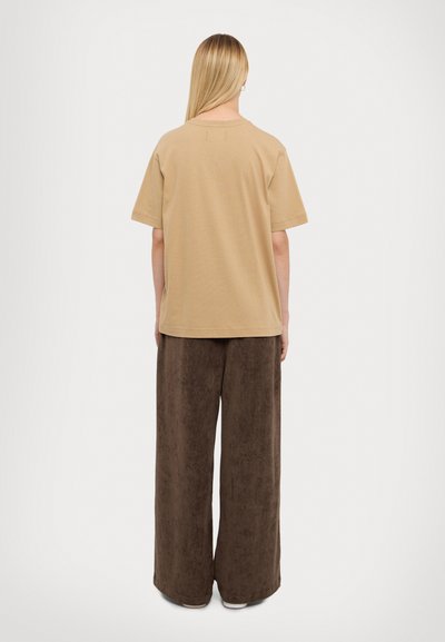 Beige relaxed-fit t-shirt with short sleeves, made of cotton. Paired with wide-legged brown pants made of soft, textured fabric.