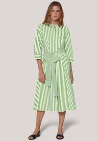 Grün-weiß gestreiftes Kleid mit kragenförmigem Ausschnitt, dreiviertel Ärmeln, Taillengürtel und knielangem Rock. Der Stoff wirkt glatt.