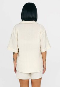 Helles beiges Kurzarmhemd aus strukturiertem Stoff mit Kragen, kombiniert mit passenden Shorts. Einfaches Design mit lockerer Passform.