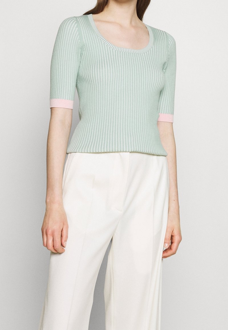 Haut en maille côtelée vert clair à manches courtes, avec des accents roses aux poignets. Le design présente un col rond et une silhouette ajustée.