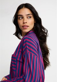 T-shirt listrada em azul escuro e rosa com mangas compridas e um bolso no peito. Tecido macio, ajuste casual, apresenta listras horizontais de larguras variadas.