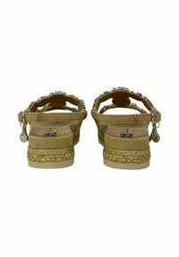 Sandali in suede beige con suola in corda di juta intrecciata, fasce decorate e dettagli metallici. La vista posteriore mostra la cinghia alla caviglia regolabile e il tacco piatto.