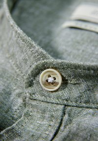 Collar de tela gris con un botón beige claro que tiene cuatro agujeros. La textura de la tela es visible, lo que resalta la suavidad y los detalles del material.