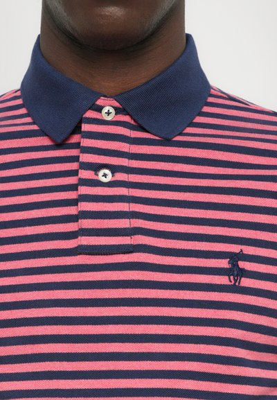 Rujuņas polo krekls ar maiņojošām rozā un tumši zila svītrām, tumši zilsapkaklītē, trīs pogu aprīkojumā un mazu logotipu uz krūtīm.