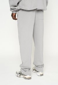 Pantalones de chándal gris claro fabricados en una mezcla de algodón, con un corte relajado, bolsillo lateral con cremallera y puños elásticos en los tobillos.