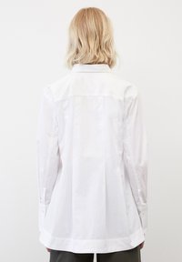 Camisa blanca de botones fabricada en algodón suave. Presenta un cuello, mangas largas y una parte trasera ligeramente acampanada para un ajuste relajado.