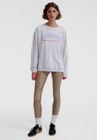Grå sweatshirt med blå och röda detaljer, tillsammans med leopardmönstrade leggings och svarta sneakers med vita inslag. Vita ankelsockor.