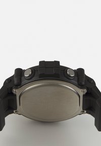 Montre en caoutchouc noir avec un dos en acier inoxydable circulaire, dotée de deux boutons argentés et d'un bracelet texturé pour une meilleure prise.