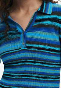 Blå och svart randig ribbad polotröja med krage, som har en tvåknappsstängning och varierande texturerade linjer i nyanser av blått och grönt.