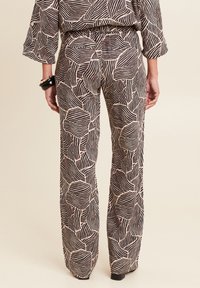 Wide-leg broek in zwart en beige met geometrisch loofpatroon, van een gestructureerde stof en een elastische tailleband. Heeft een relaxte pasvorm en minimale accenten.